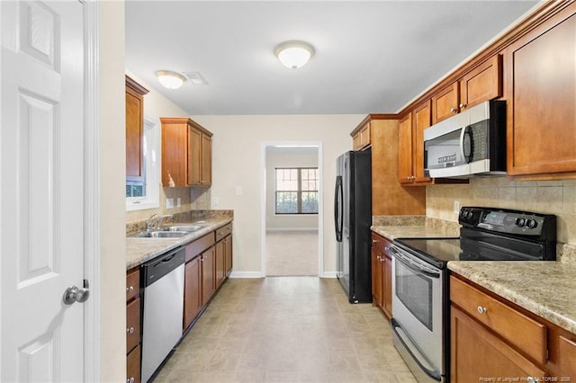 kitchen featuring brown cabinets, decorative backsplash, stainless steel appliances, and a sink