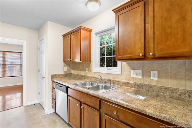 kitchen featuring light stone counters, a sink, stainless steel dishwasher, brown cabinets, and plenty of natural light