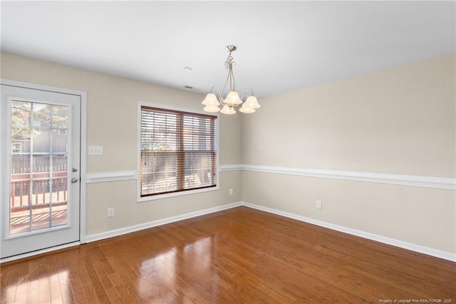 spare room featuring a notable chandelier, baseboards, and wood finished floors