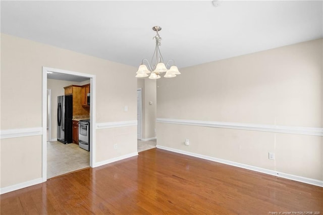 spare room featuring baseboards, wood finished floors, and an inviting chandelier