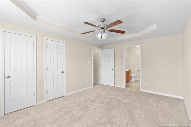 unfurnished bedroom featuring a tray ceiling, light colored carpet, baseboards, and ensuite bathroom