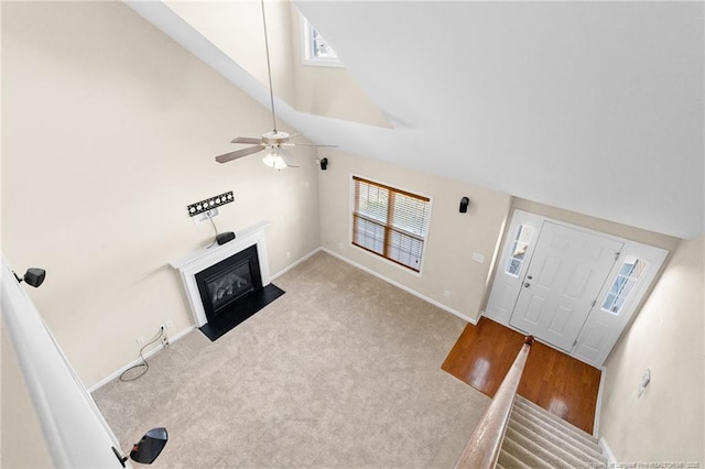 entryway with high vaulted ceiling, light carpet, a fireplace with flush hearth, a ceiling fan, and baseboards