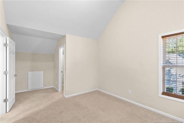 spare room featuring light colored carpet, vaulted ceiling, and baseboards