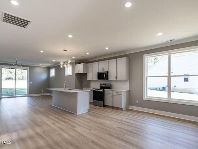 kitchen featuring light wood-type flooring, an island with sink, appliances with stainless steel finishes, decorative light fixtures, and white cabinetry