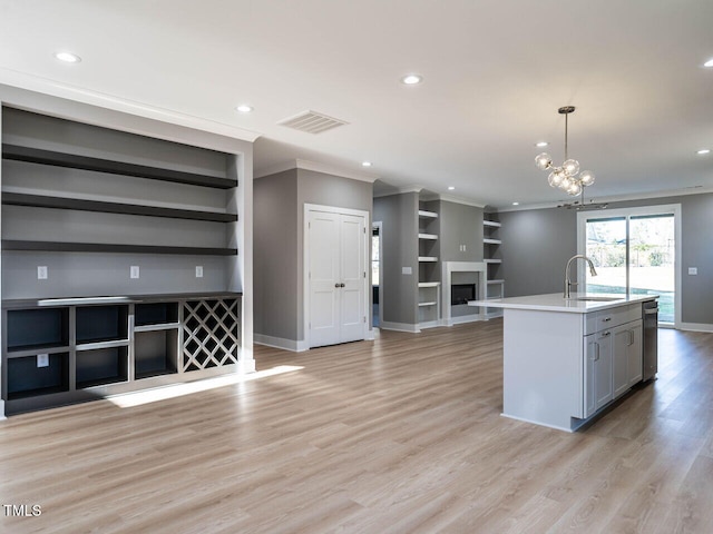 kitchen with gray cabinetry, a kitchen island with sink, sink, hanging light fixtures, and built in shelves