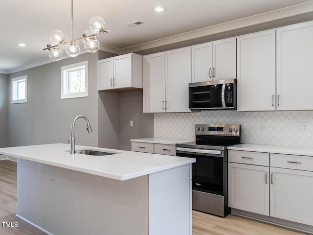 kitchen featuring a center island with sink, sink, light stone countertops, appliances with stainless steel finishes, and decorative light fixtures