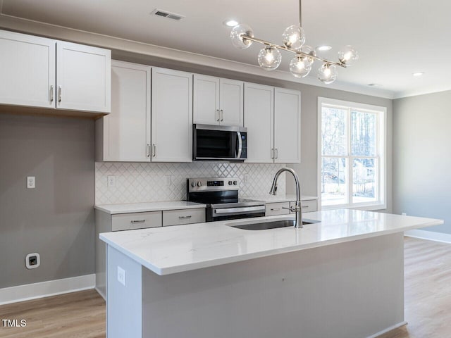 kitchen with sink, stainless steel appliances, light stone counters, an island with sink, and pendant lighting