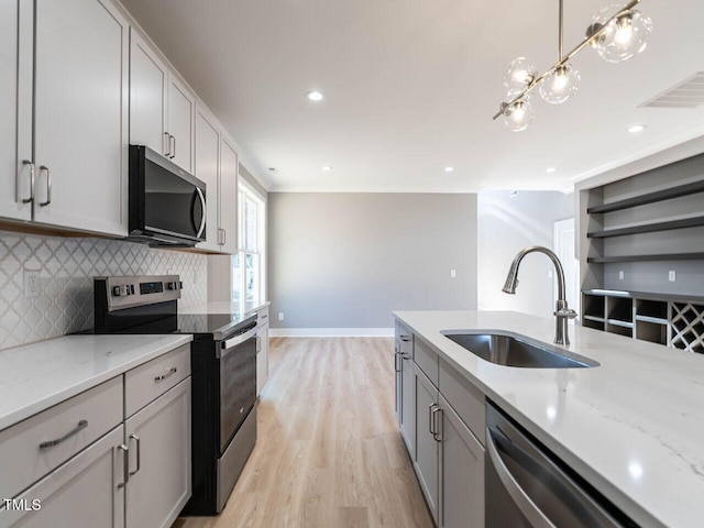 kitchen featuring pendant lighting, light stone counters, sink, and stainless steel appliances