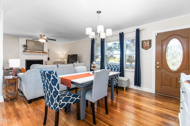 dining space featuring a fireplace, hardwood / wood-style floors, ceiling fan with notable chandelier, and crown molding