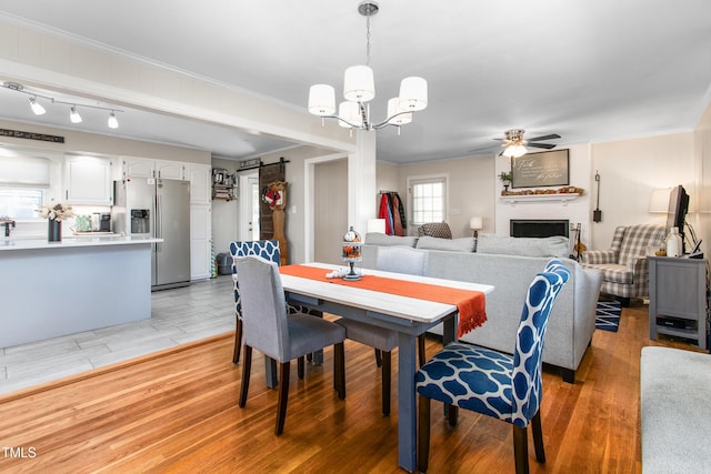 dining room with ceiling fan with notable chandelier, a barn door, light hardwood / wood-style floors, and crown molding