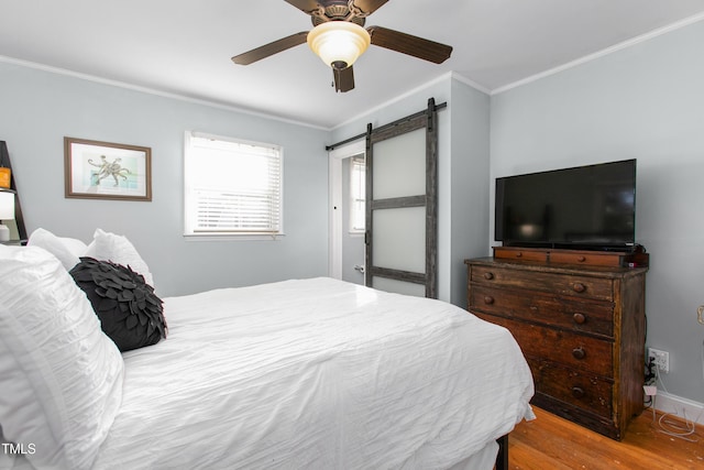 bedroom with light wood-type flooring, a barn door, ceiling fan, and crown molding