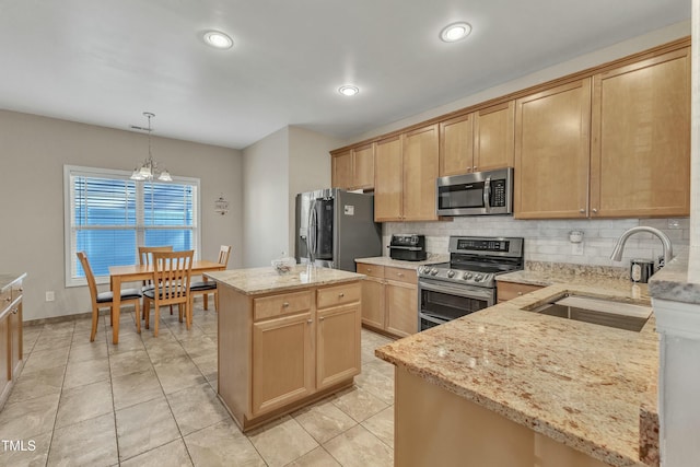 kitchen with light stone countertops, appliances with stainless steel finishes, sink, an inviting chandelier, and a kitchen island