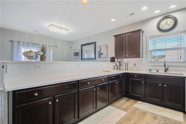 kitchen with kitchen peninsula, dark brown cabinetry, sink, and light wood-type flooring