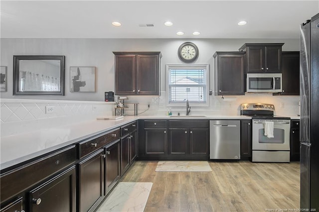 kitchen featuring dark brown cabinetry, sink, appliances with stainless steel finishes, and light hardwood / wood-style flooring