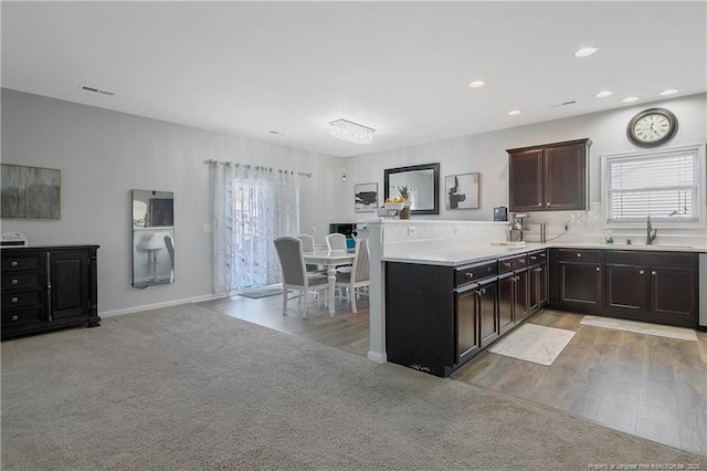 kitchen with kitchen peninsula, dark brown cabinetry, light colored carpet, sink, and a chandelier