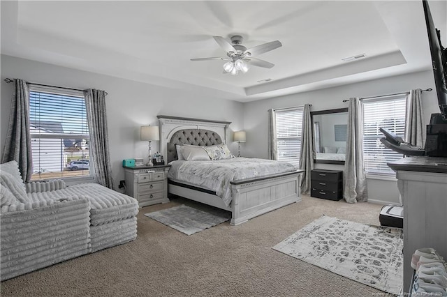 bedroom with a raised ceiling, ceiling fan, and light carpet