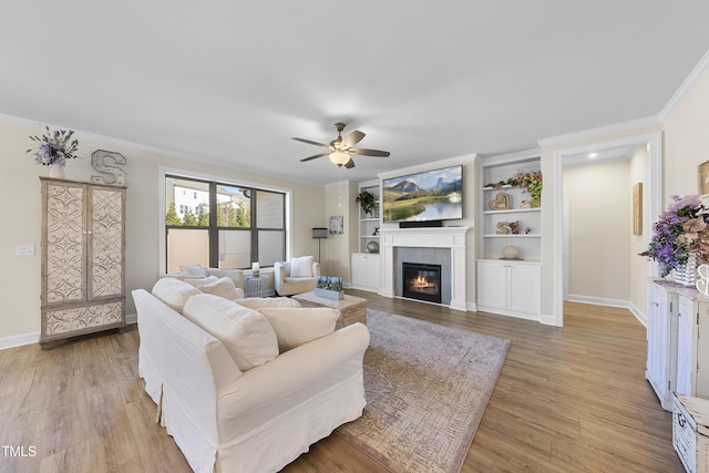 living room with built in shelves, light hardwood / wood-style floors, ceiling fan, and crown molding