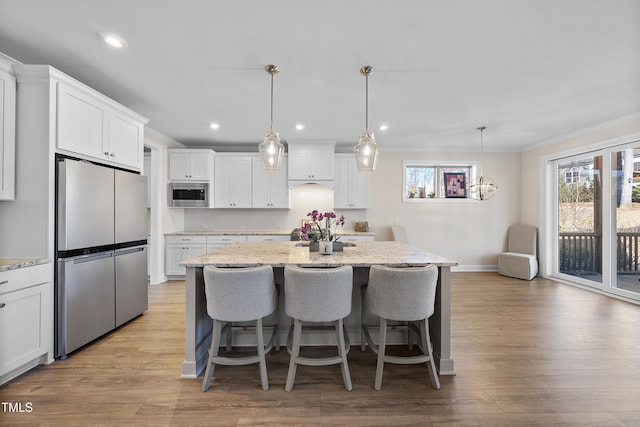 kitchen with a center island with sink, white cabinetry, hanging light fixtures, and appliances with stainless steel finishes