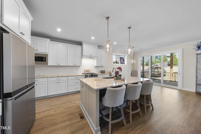 kitchen featuring light stone countertops, white cabinetry, hanging light fixtures, a kitchen island with sink, and appliances with stainless steel finishes