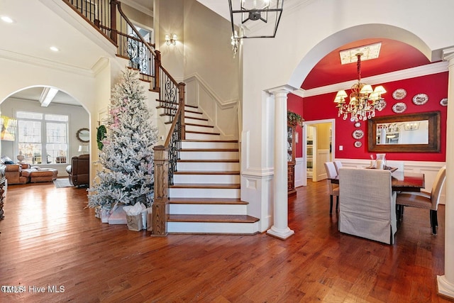 interior space featuring hardwood / wood-style floors, an inviting chandelier, a towering ceiling, beamed ceiling, and decorative columns