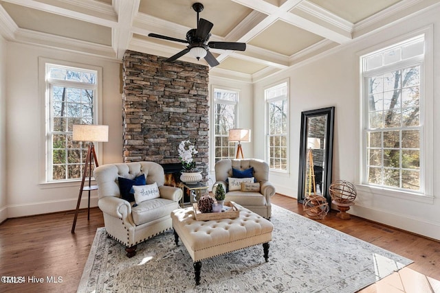 living area featuring coffered ceiling, crown molding, beamed ceiling, hardwood / wood-style floors, and a stone fireplace