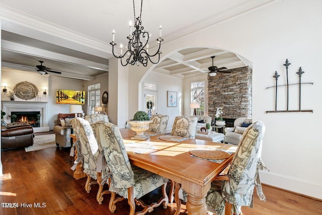 dining area with coffered ceiling, ceiling fan with notable chandelier, crown molding, beam ceiling, and a large fireplace