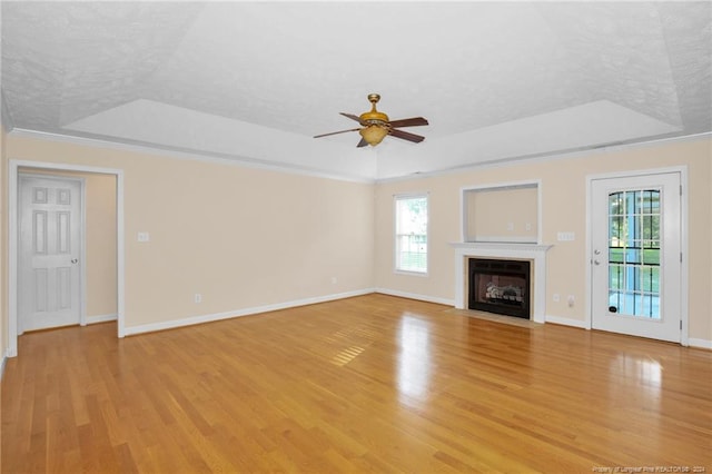 unfurnished living room with crown molding, ceiling fan, a textured ceiling, a tray ceiling, and light hardwood / wood-style floors