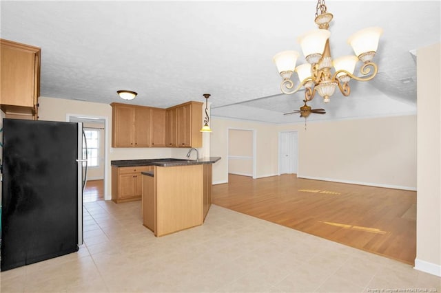 kitchen featuring kitchen peninsula, a textured ceiling, decorative light fixtures, black refrigerator, and light wood-type flooring