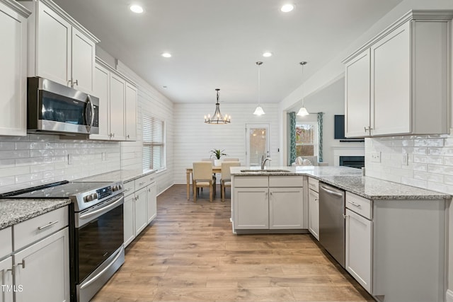 kitchen featuring sink, decorative light fixtures, light stone counters, white cabinetry, and stainless steel appliances