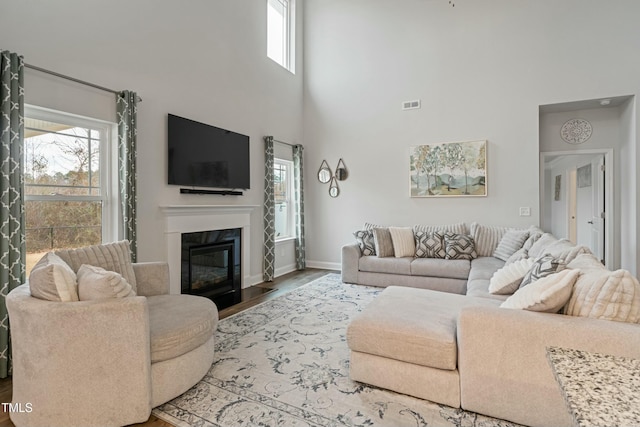 living room featuring a towering ceiling, plenty of natural light, a high end fireplace, and wood-type flooring