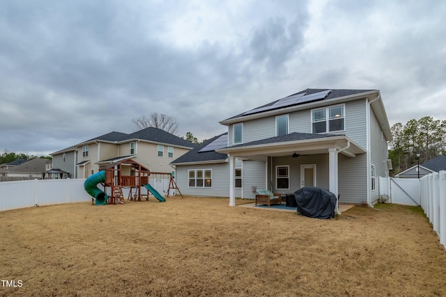 rear view of property featuring a lawn, solar panels, ceiling fan, and a playground