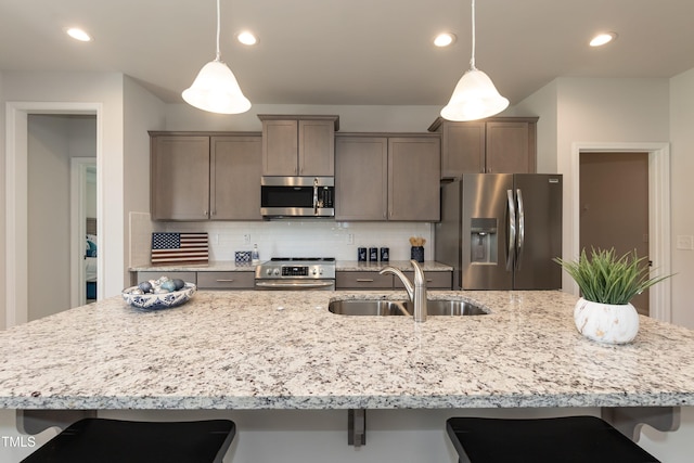 kitchen with pendant lighting, an island with sink, stainless steel appliances, and sink