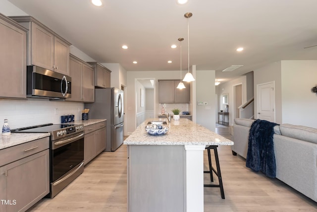 kitchen featuring a breakfast bar, a center island, light wood-type flooring, appliances with stainless steel finishes, and decorative light fixtures