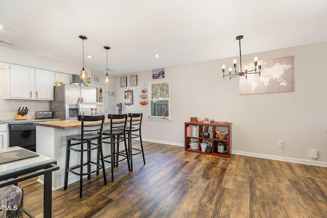 kitchen featuring pendant lighting, stainless steel fridge, black dishwasher, white cabinetry, and a breakfast bar area