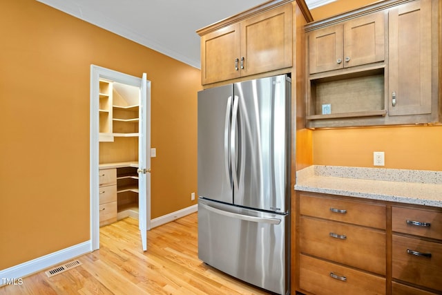 kitchen with stainless steel refrigerator, light stone counters, light hardwood / wood-style floors, and ornamental molding