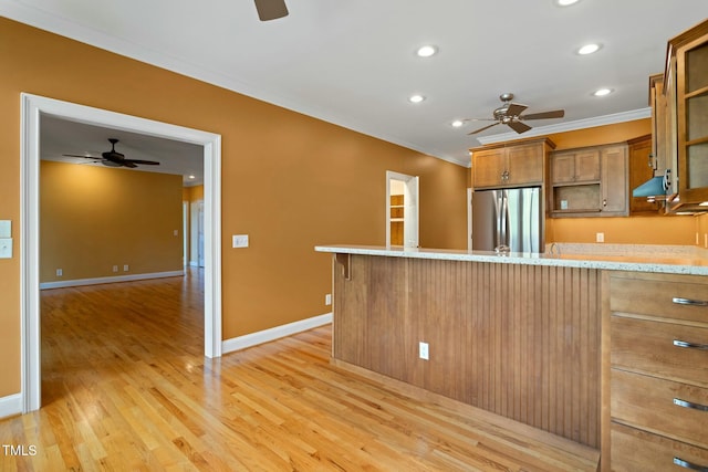 kitchen with stainless steel refrigerator, light stone countertops, ornamental molding, kitchen peninsula, and light wood-type flooring