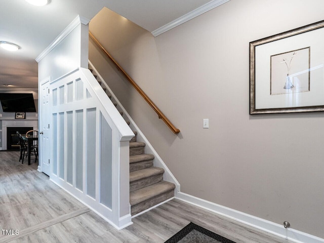 stairs featuring wood-type flooring, crown molding, and a tiled fireplace