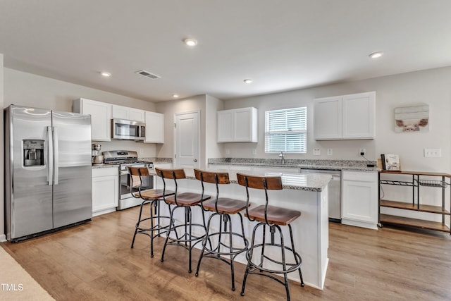 kitchen featuring white cabinets, light stone counters, appliances with stainless steel finishes, a kitchen island, and light wood-type flooring