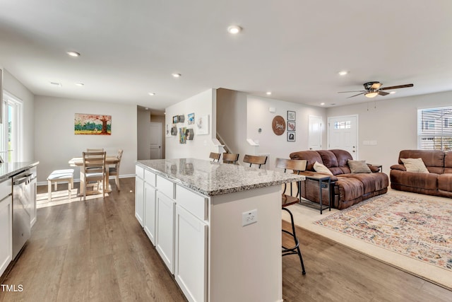 kitchen featuring a kitchen bar, stainless steel dishwasher, a kitchen island, light hardwood / wood-style flooring, and white cabinetry