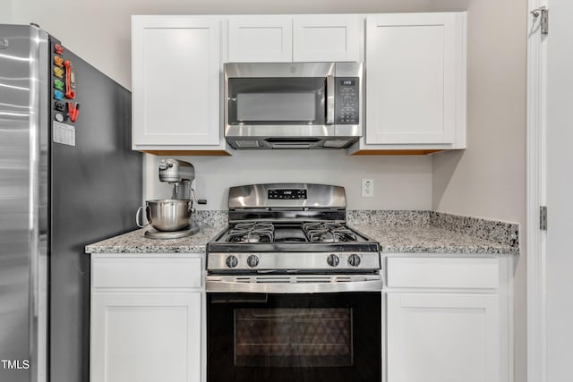 kitchen featuring light stone countertops, stainless steel appliances, and white cabinetry