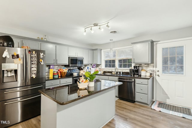 kitchen with appliances with stainless steel finishes, backsplash, gray cabinets, and a kitchen island