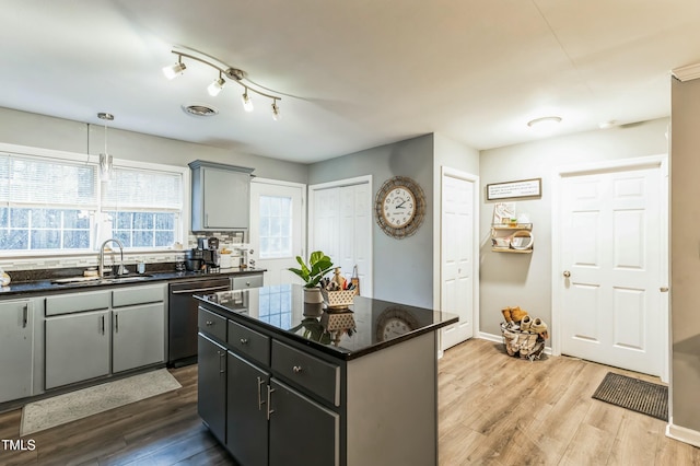 kitchen with sink, light hardwood / wood-style flooring, decorative light fixtures, dishwashing machine, and a kitchen island