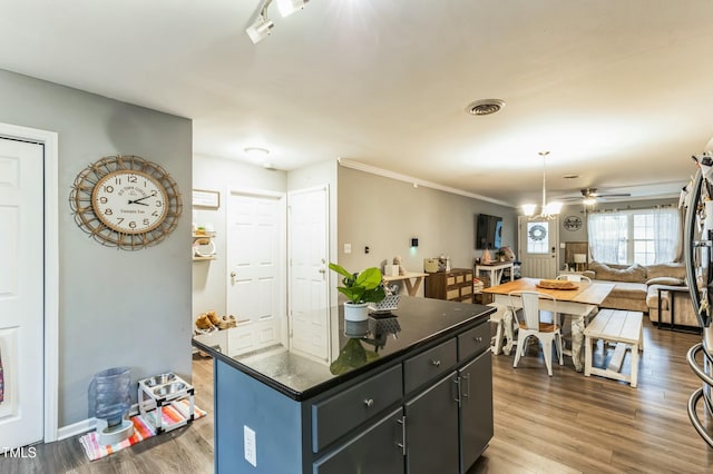 kitchen with dark hardwood / wood-style flooring, a kitchen island, ceiling fan with notable chandelier, and ornamental molding