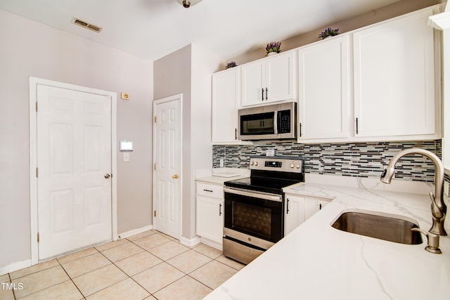 kitchen with light stone countertops, sink, stainless steel appliances, light tile patterned floors, and white cabinets