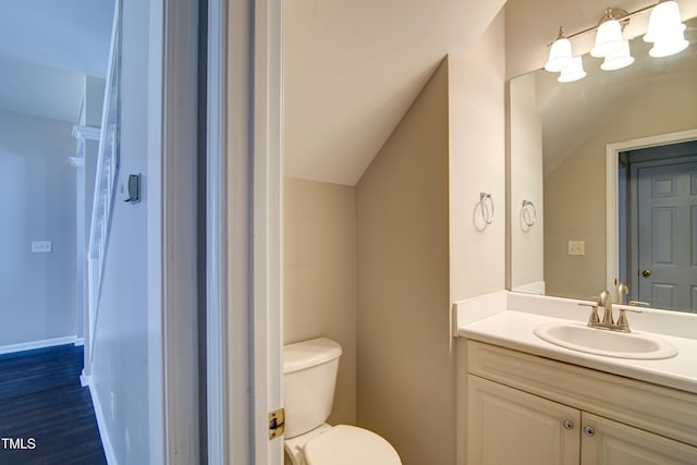 bathroom featuring vanity, wood-type flooring, lofted ceiling, and toilet