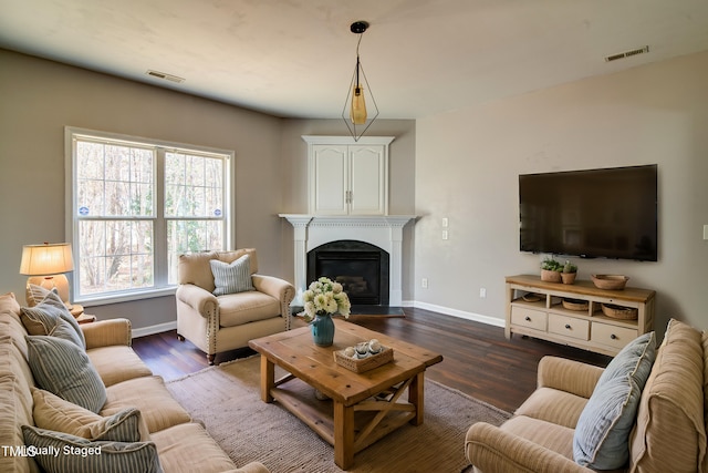 living area with visible vents, baseboards, wood finished floors, and a fireplace with flush hearth