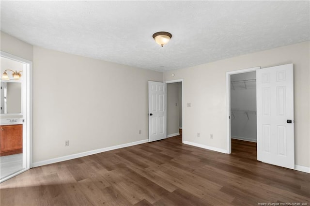 unfurnished bedroom with a walk in closet, ensuite bathroom, sink, dark hardwood / wood-style floors, and a closet