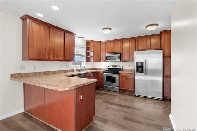 kitchen with kitchen peninsula, appliances with stainless steel finishes, dark hardwood / wood-style floors, and sink