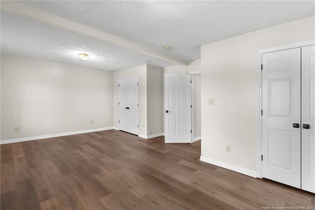 empty room featuring dark hardwood / wood-style flooring, a textured ceiling, and beam ceiling