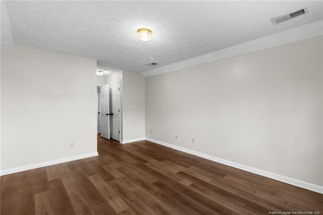 empty room featuring lofted ceiling, a textured ceiling, and dark wood-type flooring